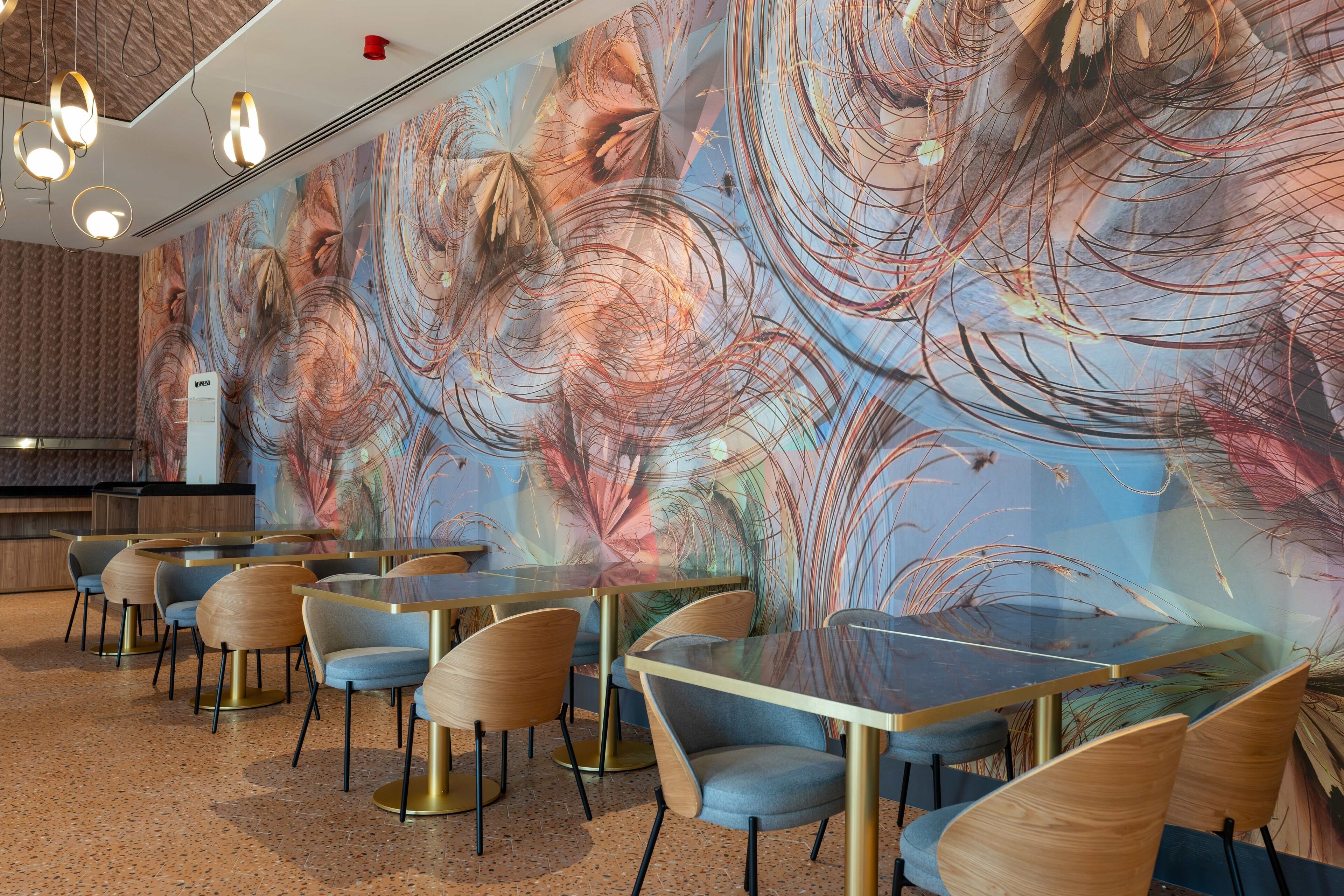 Un interno ristorante moderno con tavoli e sedie rotonde, un'ampia murale astratta sulla parete e un pavimento maculato.