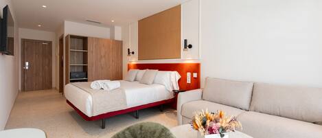 A modern hotel room with a bed, a sofa, a small table with a vase of flowers, and a wooden wardrobe.