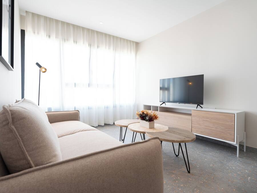Una sala de estar moderna con un sofá, un televisor, una mesita con un florero y una lámpara.