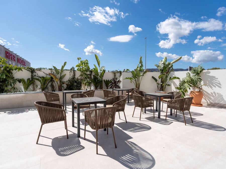 An outdoor patio with tables and chairs, surrounded by potted plants and a clear blue sky.
