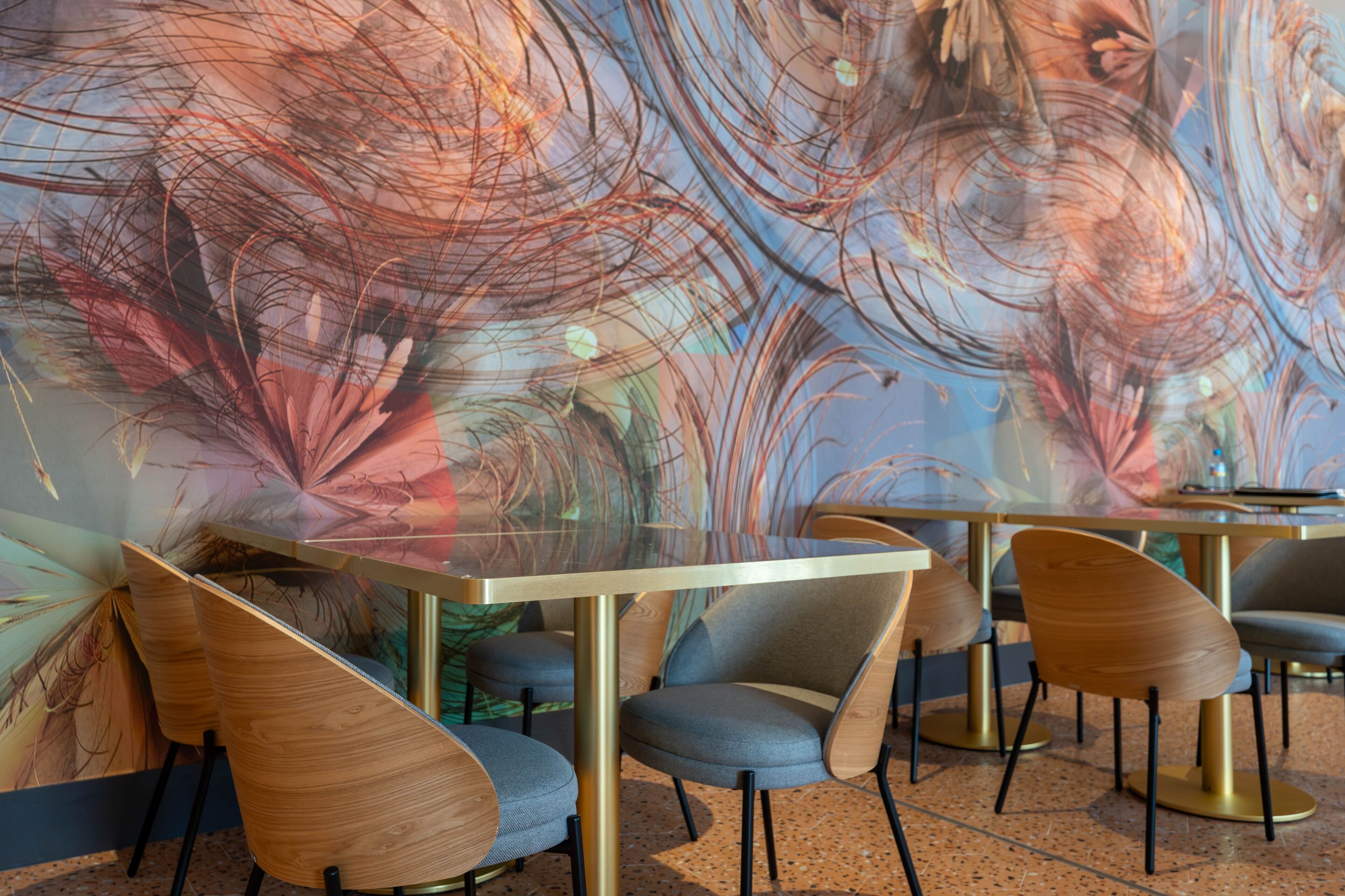 Een modern interieur met abstracte wanddecoratie, houten en gestoffeerde stoelen en een tafel met een glazen blad.