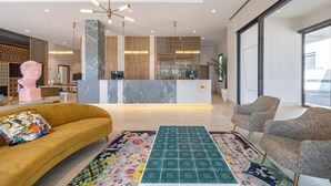 Un vestíbul d'hotel modern amb una recepció, un sofà, estores estampades i una finestra gran.