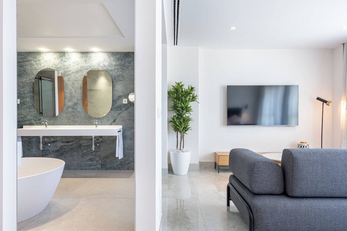 A modern bathroom with a large bathtub, a double sink, and a potted plant.
