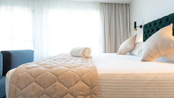 Una habitación de hotel con una cama, un sillón azul y un ventanal con cortinas.