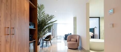Una sala de estar moderna con un mueble de madera, una planta grande en maceta, un sillón color beige y una mesa de centro de vidrio.