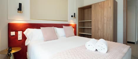 Une chambre d’hôtel avec un grand lit, une armoire en bois, une table de chevet et un luminaire fixé au mur.