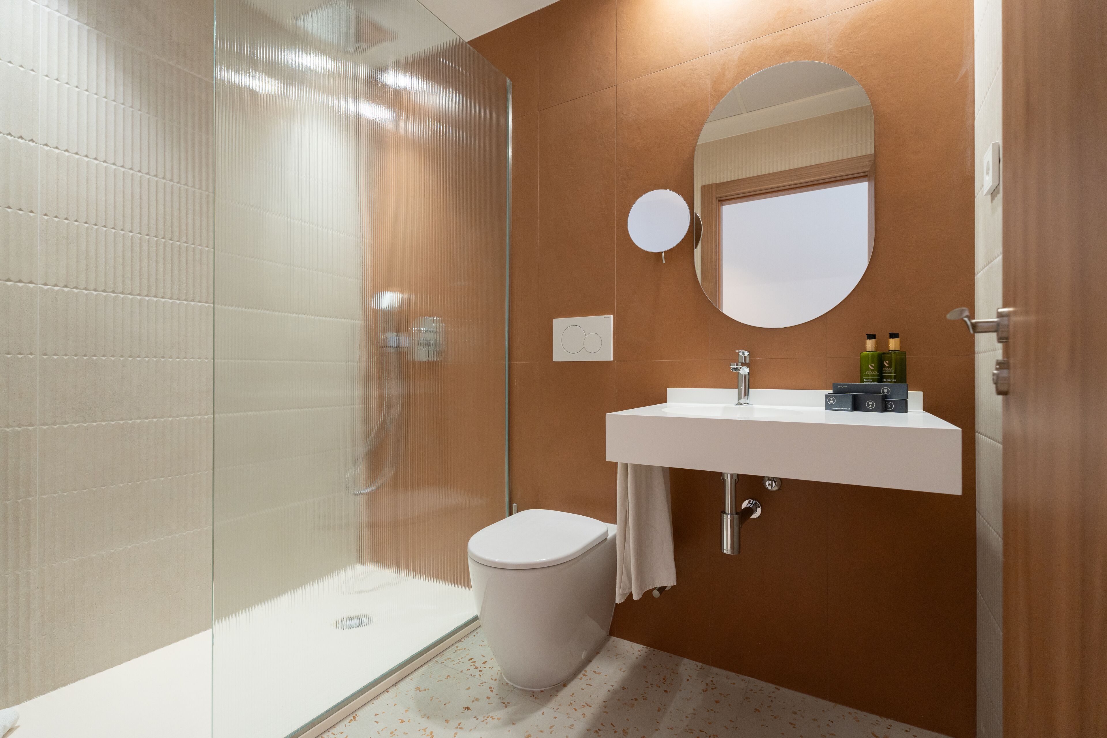 A modern bathroom with a glass-enclosed shower, a white toilet, and a white sink with a mirror above it.