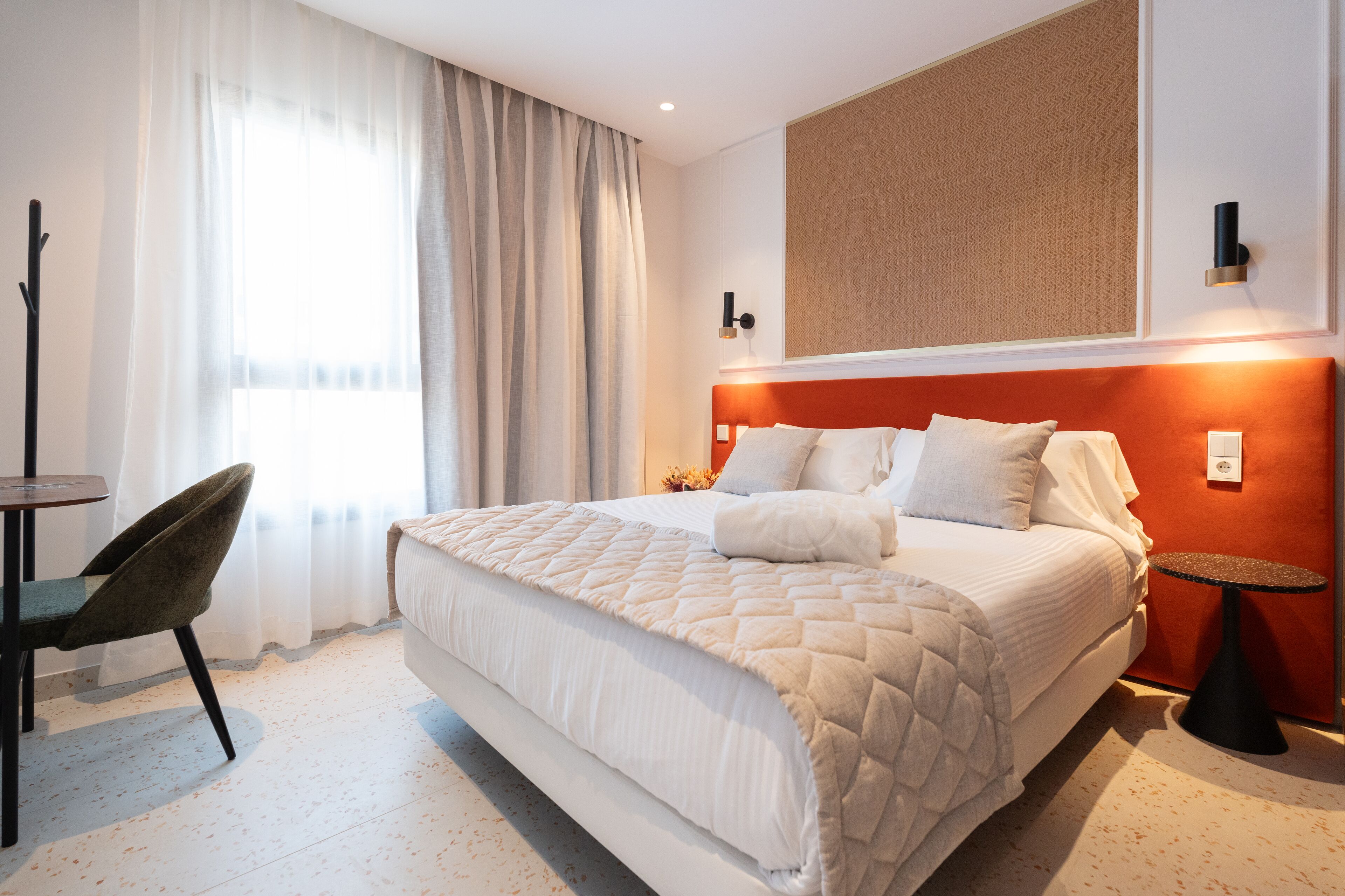 Een hotelkamer met een groot bed, een stoel, een tafeltje en een wandlamp.