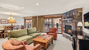A living room with a fireplace, a sofa, two armchairs, a coffee table, and a dining area with a wooden table and chairs. - North Of Nell, Unit 2e (Aspen)