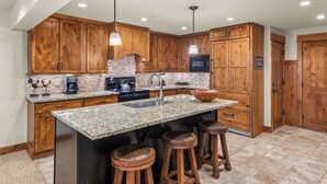 A kitchen with wooden cabinets, granite countertops, a built-in microwave, and a large island with stools. - North Of Nell, Unit 2e (Aspen)