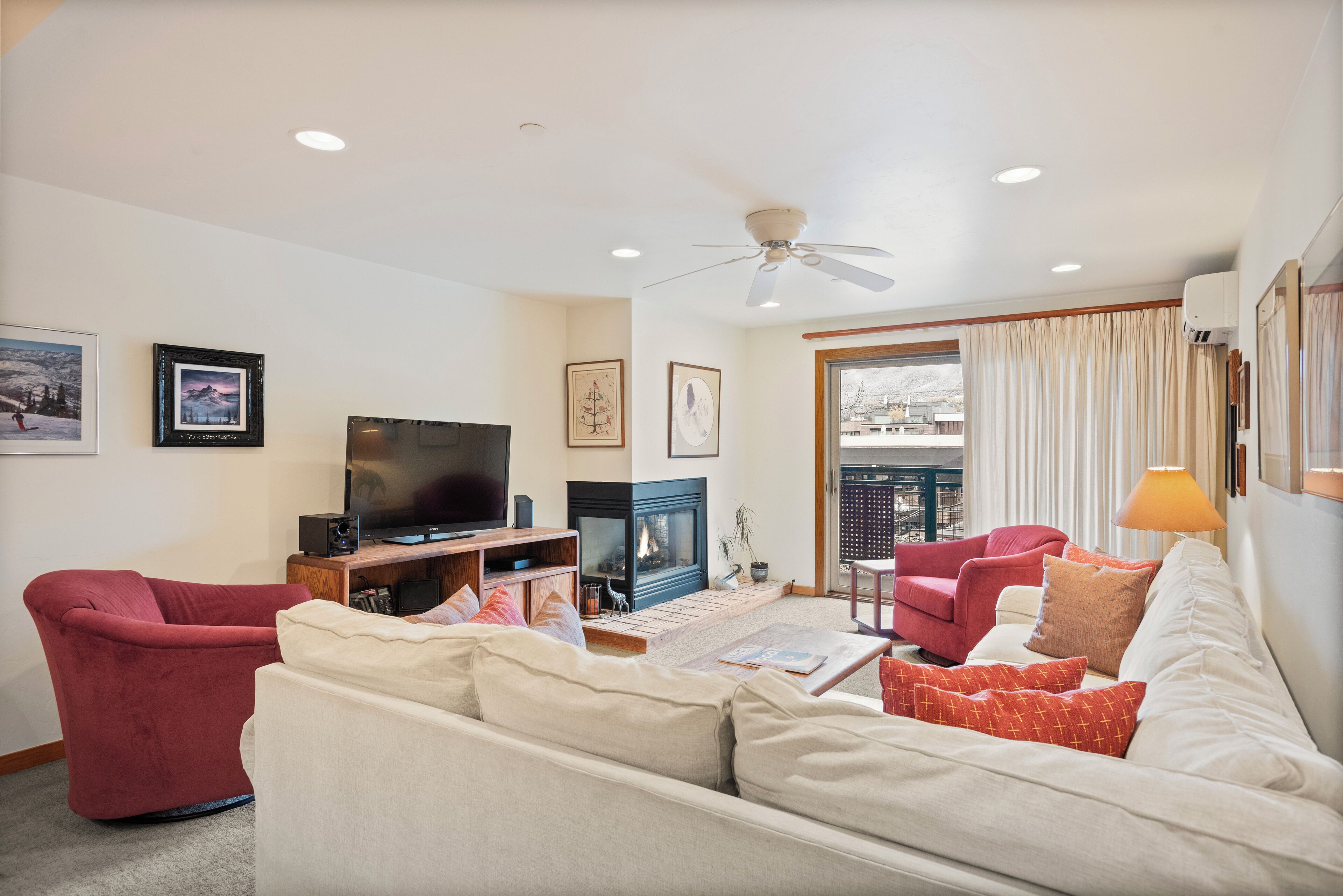 A living room with a sofa, chairs, a TV, a fireplace, and a ceiling fan.