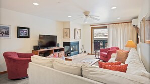 A living room with a sofa, chairs, a TV, a fireplace, and a ceiling fan. - North Of Nell, Unit 2m (Aspen)