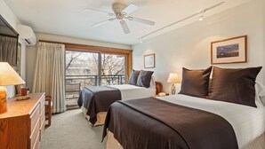 A hotel room with two beds, a ceiling fan, a large window with curtains, a wooden dresser, and a framed picture on the wall. - North Of Nell, Unit 2m (Aspen)