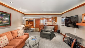 A modern living room with a sofa, armchair, and glass coffee table. A flat-screen TV and wooden entertainment unit are on the wall. - North Of Nell, Unit 3f (Aspen)