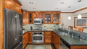 A modern kitchen with wooden cabinets, stainless steel appliances, a tiled backsplash, and a granite countertop. - North Of Nell, Unit 3f (Aspen)