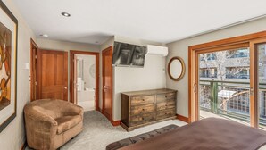 A bedroom with a large bed, a wooden dresser, a TV mounted on the wall, and a balcony with a view of the city. - North Of Nell, Unit 3f (Aspen)