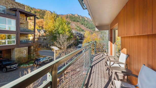 A balcony with a view of a mountain, a car parked outside, and a building with a wooden facade. - North Of Nell, Unit 3f (Aspen)