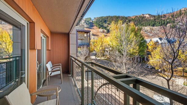 Un balcon offrant une vue sur un paysage montagneux, un mur extérieur en bois et un coin salon avec deux chaises.