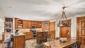 A spacious kitchen with wooden cabinets, a central island, and a dining area with a large wooden table and bar stools. - North Of Nell, Unit 3i (Aspen)