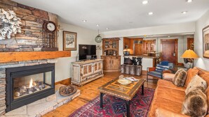 A spacious living room with a stone fireplace, wooden cabinets, a television, and a cozy seating area. - North Of Nell, Unit 3i (Aspen)