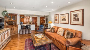 A spacious living room with a brown leather sofa, wooden coffee table, and a patterned rug. A dining area with a table and chairs is visible in the background. - North Of Nell, Unit 3i (Aspen)