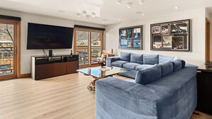 A modern living room with a blue sofa, a glass coffee table, and a large flat-screen TV mounted on the wall. - North Of Nell, Unit 3j (Aspen)