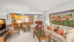 A spacious living room with a sofa, armchairs, and a coffee table. A kitchen is visible in the background. - North Of Nell, Unit 3L (Aspen)