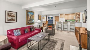 A spacious living room with a red sofa, a coffee table, and a kitchen area in the background.