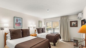 A hotel room with two beds, a window with curtains, a lamp, and a framed picture on the wall.