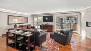 A modern living room with a sofa, coffee table, and TV. There is a bookshelf and a window with a view. - North Of Nell, Unit 4e (Aspen)