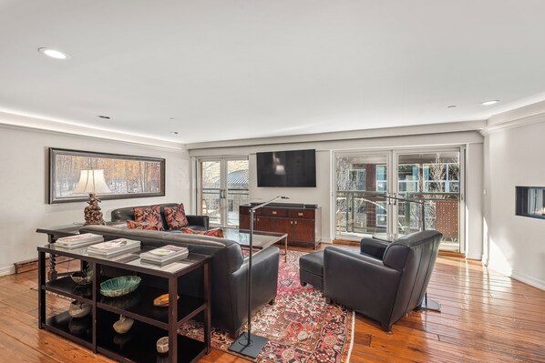 A modern living room with a sofa, coffee table, and TV. There is a bookshelf and a window with a view. - North Of Nell, Unit 4e (Aspen)
