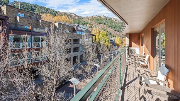 A balcony with outdoor seating, overlooking a building with multiple floors and a mountainous backdrop. - North Of Nell, Unit 4e (Aspen)