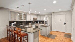 A modern kitchen with a central island, wooden bar stools, stainless steel appliances, and recessed lighting. - North Of Nell, Unit 4e (Aspen)