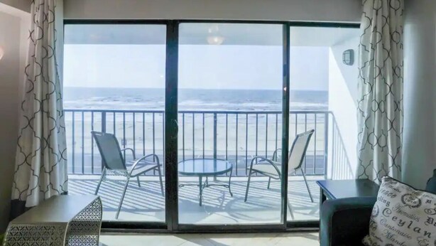 A balcony with a view of the ocean, two chairs, and a small table.