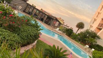 A swimming pool with lounge chairs, surrounded by greenery and palm trees.