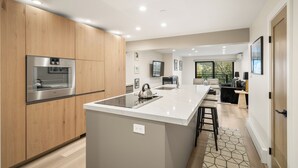 A modern kitchen with wooden cabinets, a stainless steel refrigerator, and a central island with a kettle. - North Of Nell, Unit 4h (Aspen)