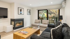 A modern living room with a fireplace, comfortable seating, and a large window offering a view of trees. - North Of Nell, Unit 4h (Aspen)