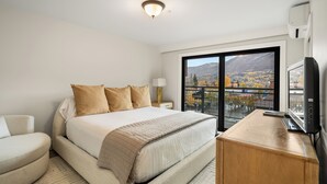 A hotel room with a large bed, a desk, a TV, and a view of a cityscape through a large window. - North Of Nell, Unit 4h (Aspen)