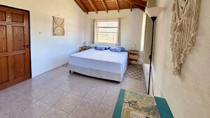 A bedroom with a wooden ceiling, a bed with patterned bedding, a window with curtains, and a macrame wall hanging. - Entire Villa with Pool, Ocean View & A/C - 5min to beach and Culpepper Spring (St. Philip)