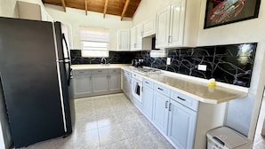 A kitchen with white cabinets, a black refrigerator, a marble backsplash, and a ceiling with exposed wooden beams. - Entire Villa with Pool, Ocean View & A/C - 5min to beach and Culpepper Spring (St. Philip)