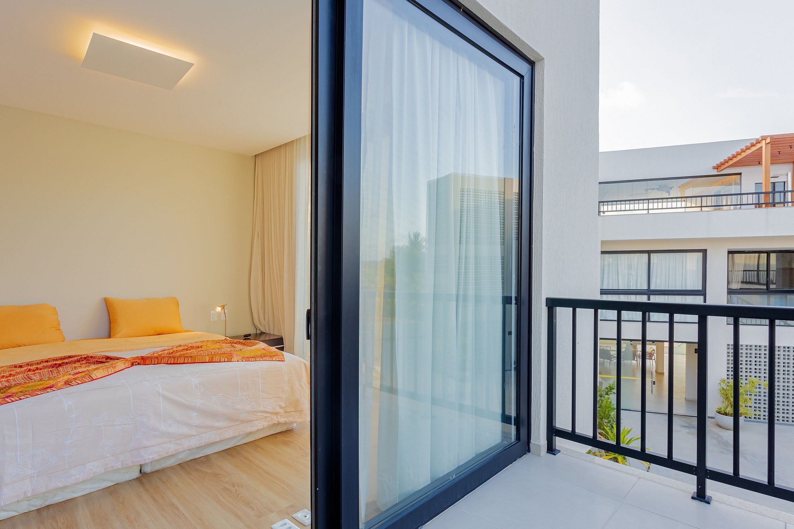 Une chambre moderne avec un grand lit, une porte-fenêtre coulissante donnant sur un balcon et une vue sur le paysage urbain.