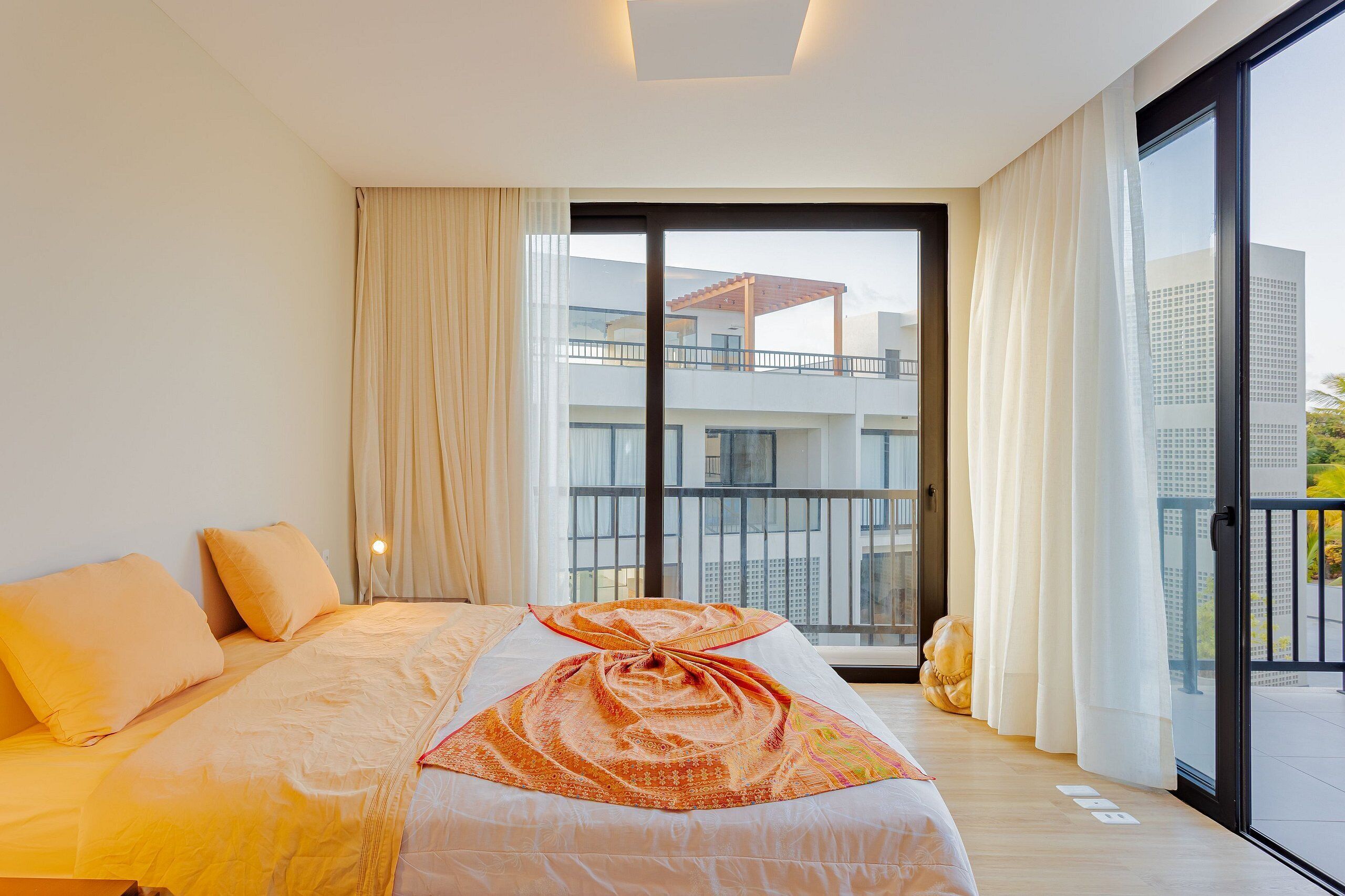 A hotel room with a large bed, a view of a balcony, and a cityscape in the background.