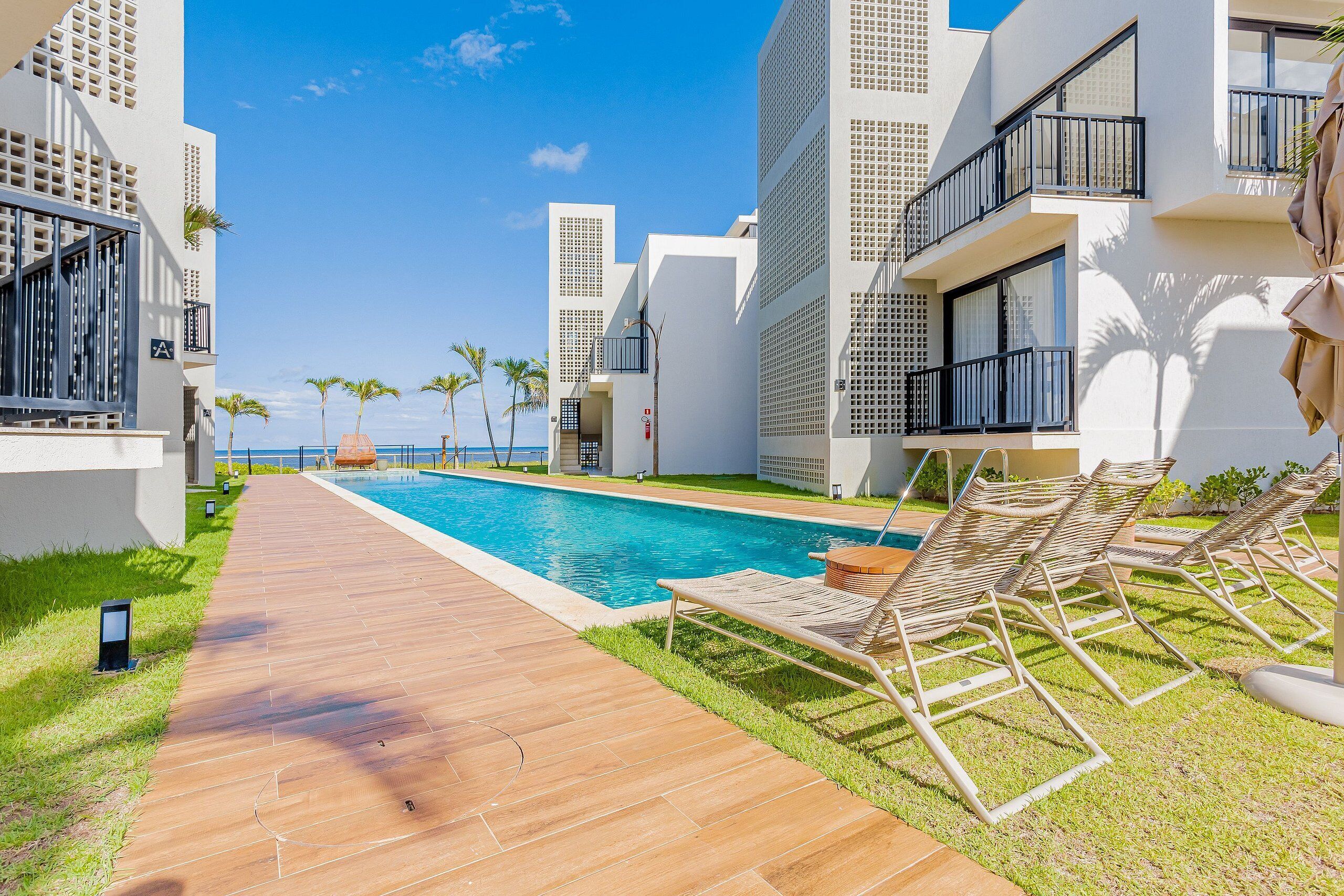 Un hôtel moderne doté d’une piscine, de chaises longues et offrant une vue sur l’océan.