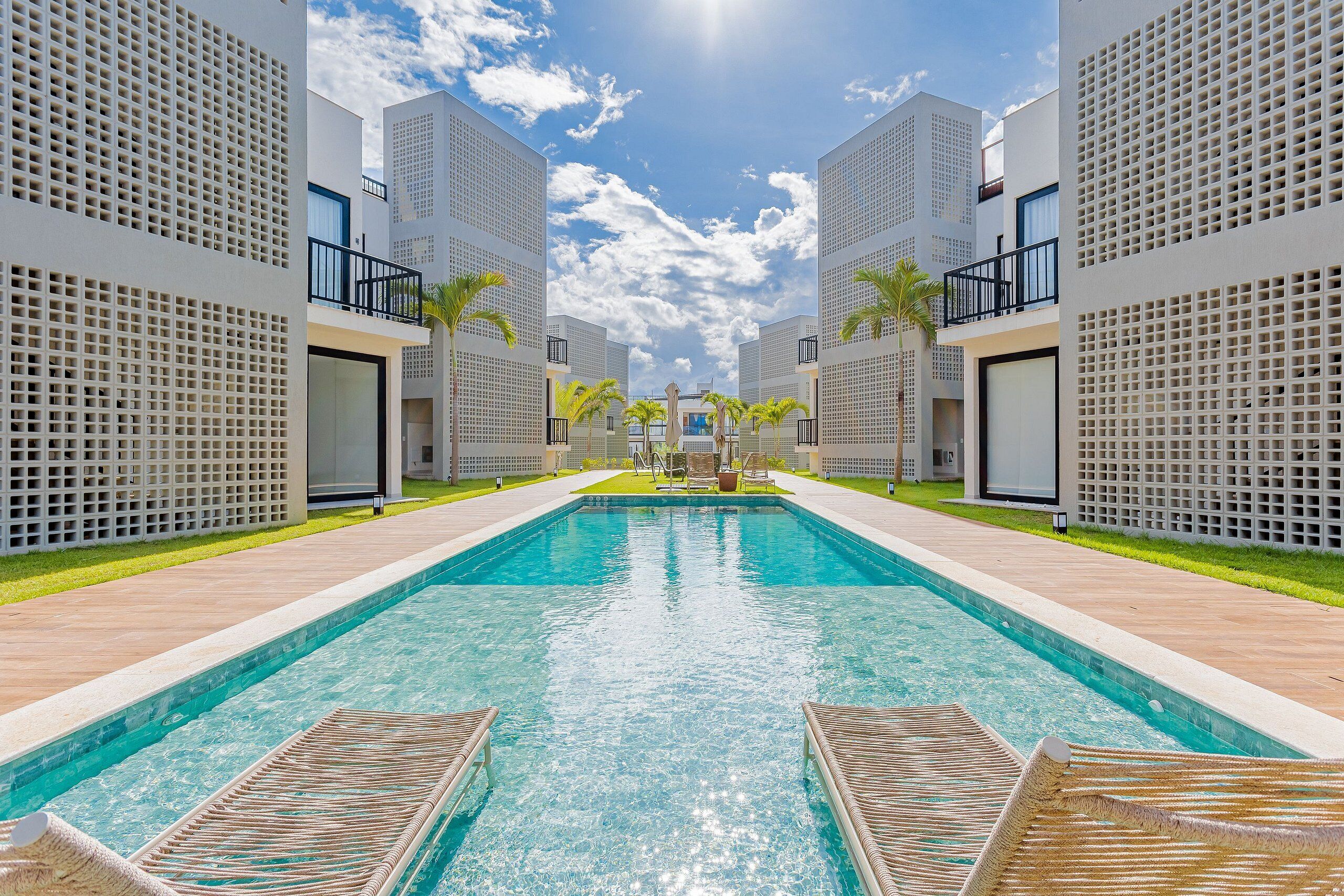 A swimming pool with lounge chairs, surrounded by modern buildings with balconies and a clear sky.