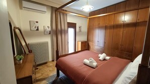 A bedroom with a large bed, wooden wardrobe, radiator, and artwork on the wall. - Deluxe Family Suite - Kalabaka (Kalabaka)