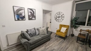 A living room with a grey sofa, a yellow armchair, and a round wall clock. - The road to Wigan Pier (Wigan)