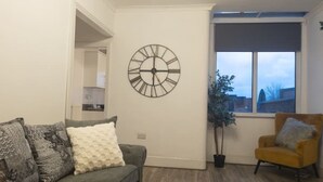 A living room with a modern clock, a sofa, a chair, and a window with a view. - The road to Wigan Pier (Wigan)
