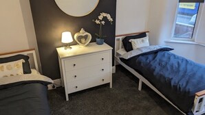 A bedroom with a bed, a bedside table with a lamp, a dresser, and a wall-mounted picture. - The road to Wigan Pier (Wigan)
