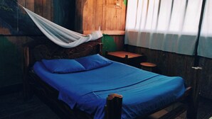 A bed with a blue mattress and pillows, a wooden headboard, a wooden wall, a small round table, and a white hanging chair. - Hospedaje  Reina Arriera Amazonas  (Leticia)