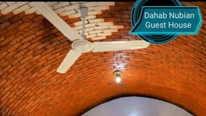 A guest room with a brick ceiling, an air conditioning unit, a bed with pillows, and a window with curtains. - Dahab Guest House (Aswan)